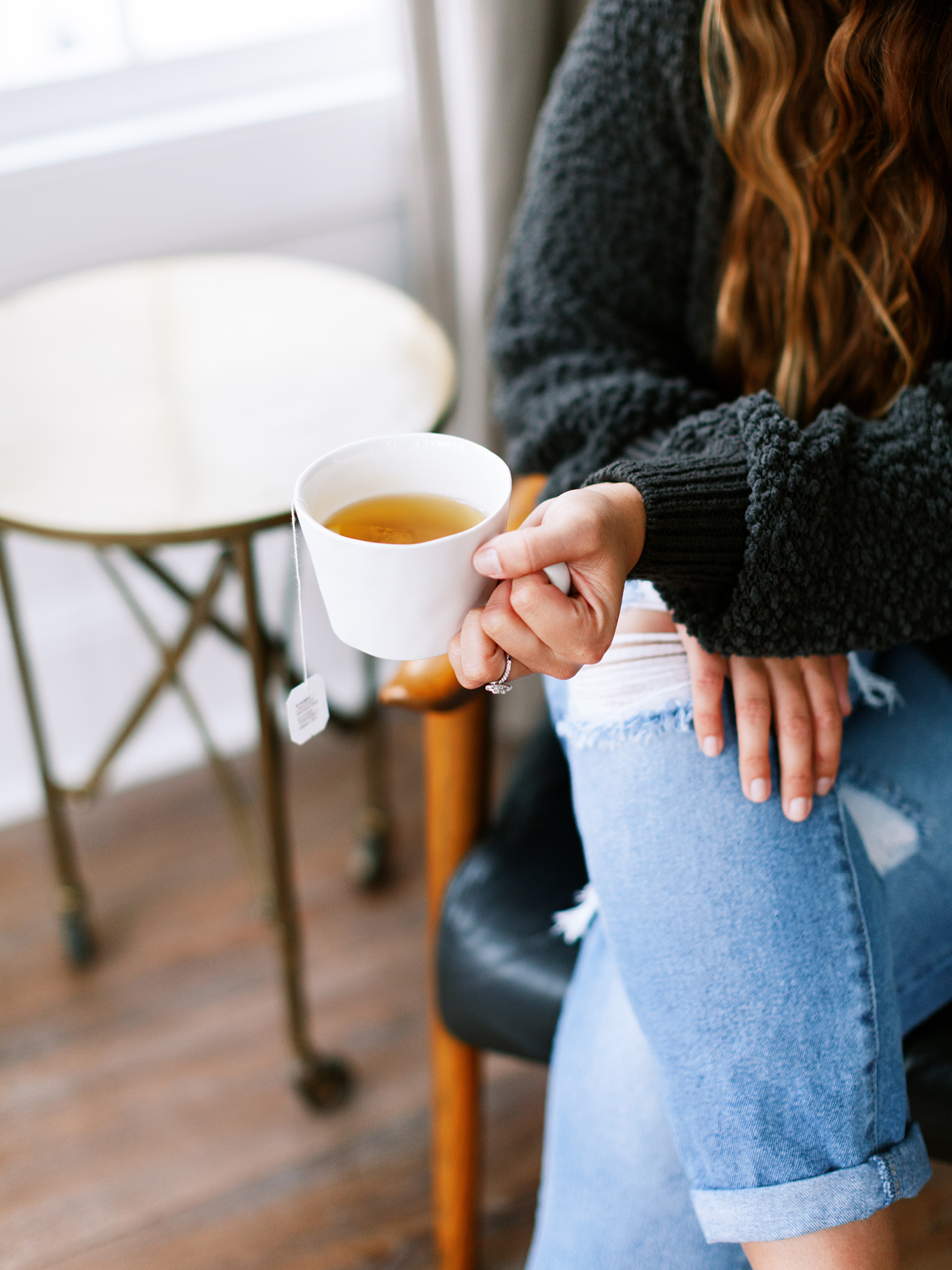 A contemplative woman in her 60s with anxiety sitting by a window with soft morning light
